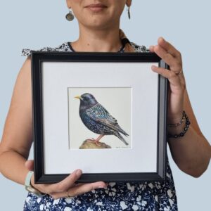 The artist holding the framed starling illustration